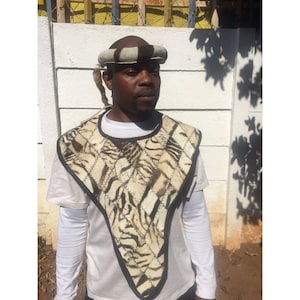 May include: A man wearing a white shirt and a traditional zebra-print garment with a black leather trim. He is also wearing a white and black headband.