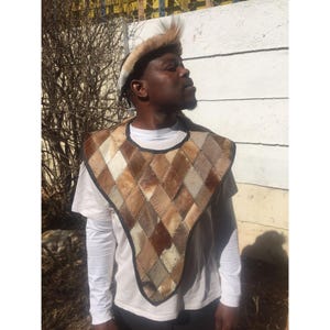 May include: A brown and tan leather vest with a diamond pattern. The vest is made of many small pieces of leather sewn together. The vest has a black leather trim around the edges.