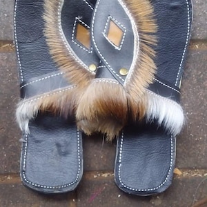 May include: A pair of black leather sandals with fur trim. The sandals have a white stitching detail and a brown leather accent.