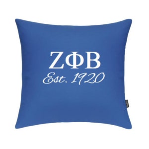 May include: A square, royal blue pillow with white text. The text includes the Greek letters Z, Φ, and B, along with "Est. 1920". The pillow is a solid color with a simple, clean design.