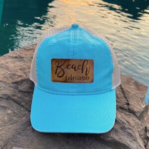 May include: A turquoise blue and white mesh baseball cap with a brown leather patch that says "Beach please".
