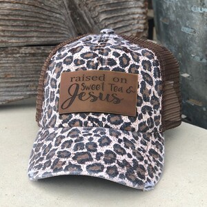 May include: Brown and white leopard print trucker hat with a brown leather patch that says "raised on sweet tea & Jesus".