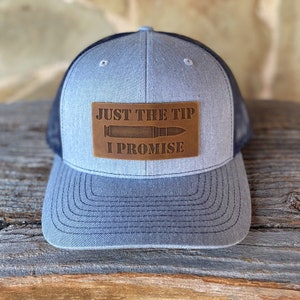 May include: A gray and black trucker hat with a brown leather patch that says "JUST THE TIP I PROMISE" with a bullet graphic.