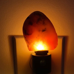 May include: A warm orange agate night light plugged into an electrical outlet. The agate is translucent and glows from within.