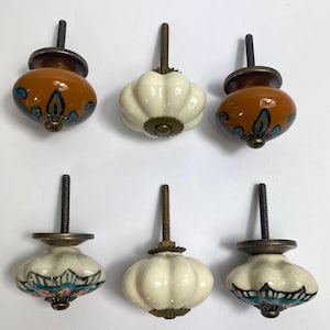 May include: Six ceramic cabinet knobs in a variety of designs. Two are orange with blue and teal floral patterns, two are white with a scalloped shape, and two are white with blue and pink floral designs. Each has a metal screw.