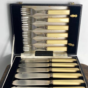 May include: A set of six silver forks and six silver knives with ivory-colored handles in a black velvet-lined case.