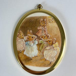 May include: An oval-shaped, gold-framed artwork featuring a watercolor illustration of several mice in vintage clothing. The mice are gathered in a room, some dancing. The artwork has a cream-colored background and a gold frame.
