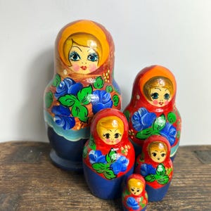 Peut inclure: Ensemble de cinq poupées russes, ou Matriochkas, de tailles variées. Les poupées présentent des visages peints et des motifs floraux bleus, verts et rouges sur une base bleue. La plus grande poupée mesure environ 15 cm de haut.