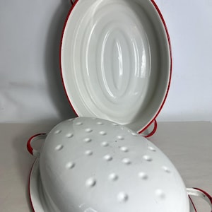 May include: White enamel oval roaster with red trim and handles. The roaster has a lid with small holes and a matching oval base. A classic kitchenware item.