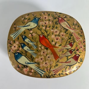 May include: Oval-shaped decorative box with a gold background and a painted design of birds and pink flowers. The birds are in shades of blue, red, and white. The box has a glossy finish.