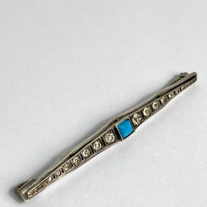 May include: A silver bar pin with a turquoise stone set in the center and surrounded by small diamonds.