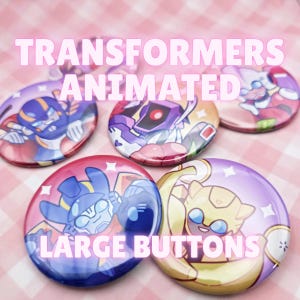 Puede incluir: Una colección de cinco botones grandes y redondos con personajes de Transformers Animated. Los botones tienen un acabado brillante y colores vibrantes, con el texto "TRANSFORMERS ANIMATED LARGE BUTTONS". El fondo es un patrón de cuadros rosas y blancos.