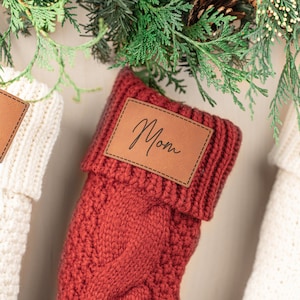 May include: Red knitted Christmas stocking with a brown leather tag that says "Mom".