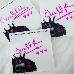 May include: Three white square stickers featuring a black and purple skull with a crown on top and roses surrounding it. Each sticker has a pink signature that reads "Elena A. Reyes" and three pink hearts. The text "https://www.elenareyes.com" is printed on two of the stickers.