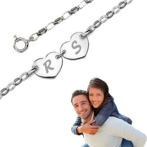 Op de afbeelding: Een zilveren kettingarmband met twee hartvormige bedels. De bedels zijn gegraveerd met de letters "R" en "S".
