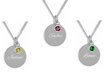 May include: Three silver necklaces with round pendants. Each pendant has a different colored gemstone and a name engraved on it: Julian with a yellow gemstone, Sophie with a red gemstone, and Leonie with a green gemstone.