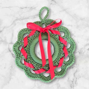May include: A green crocheted wreath with a red ribbon bow. The wreath is decorated with a red ribbon that is woven through the crocheted design.