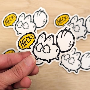 May include: White cartoon sticker of a surprised creature with large eyes and a fluffy tail. The sticker has a yellow speech bubble with the word "HECK!" in black. Several stickers are visible.
