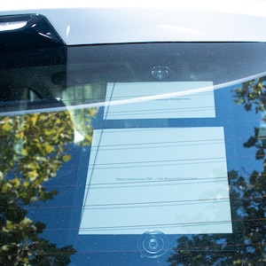 May include: A white paper form with the text "Place sticker for "TRIP" + CHI Airport Permit Sign" is attached to the rear window of a car with a suction cup.