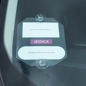 Könnte beinhalten: Ein transparenter Aufkleber aus Kunststoff für die Windschutzscheibe mit dem Text "Place stick your Rideshare Emblem here" und "Place stick your official Rideshare Emblem here". Der Aufkleber hat auch ein rosa Rechteck mit dem Namen "JESSICA" darauf gedruckt.