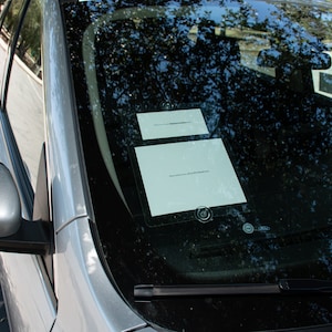 May include: A silver car windshield with two white pieces of paper with text on them. The text on the bottom piece of paper reads "Please notify you if you find this brochure".