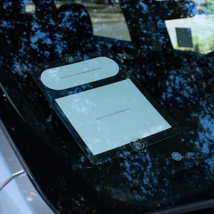 May include: A white sign with black text on a car windshield. The sign says "Please collect your offering at the Welcome Center" and "Please enter your phone number here".