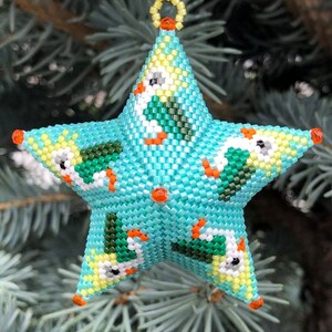 May include: A turquoise blue star-shaped Christmas ornament with a beaded design featuring white and green birds. The ornament has a loop at the top for hanging.