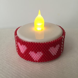 May include: A red and pink beaded tea light holder with a white tea light inside. The tea light is lit and glowing.