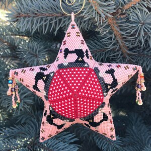 May include: A pink star-shaped Christmas ornament with a red and white ladybug design. The ornament is beaded with a gold wire hanger.