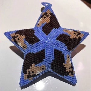 May include: A blue star-shaped ornament with a repeating pattern of brown and beige faces. The ornament is made of beads and has a loop at the top for hanging.