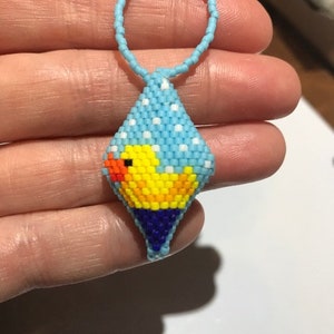 May include: A blue and white beaded ornament featuring a yellow rubber ducky design. The ornament has a loop at the top for hanging.