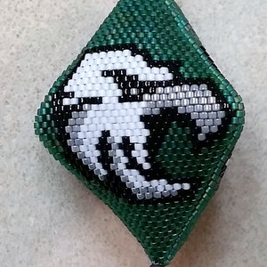 May include: A green and white beaded ornament with a white and black design of a creature. The ornament is shaped like a diamond and has a silver cord.