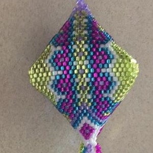 May include: A colorful beaded ornament with a diamond-shaped design and a long tassel. The ornament is made with white, green, blue, pink, and purple beads.