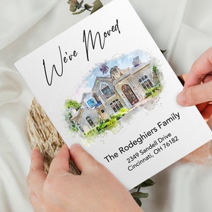 A personalized "We've Moved" announcement card featuring a custom watercolor illustration of a house, held by two hands against a soft white fabric background. The text includes the family name and a Cincinnati, Ohio address.