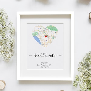 May include: A framed print featuring a heart-shaped map of Los Angeles, CA, with a red marker. The names "brad & moly" are written in cursive, with the text "Engaged Los Angeles, CA 12/27/2011" below.