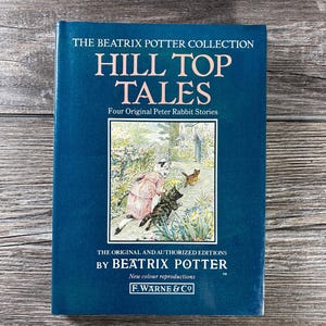 May include: A hardcover book titled "Hill Top Tales" from The Beatrix Potter Collection. The cover is a deep blue with white text and a color illustration of Peter Rabbit. The book is an original and authorized edition by Beatrix Potter.
