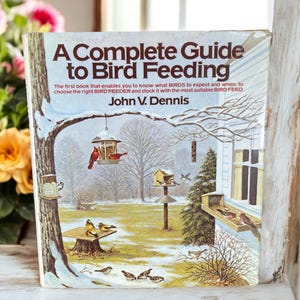 May include: A vintage book cover with a snowy winter scene featuring a bird feeder and various birds. The title is "A Complete Guide to Bird Feeding" by John V. Dennis.