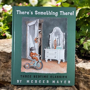 May include: A hardcover children's book titled "There's Something There!" in green with an illustration of a child on a tricycle and a monster in a doorway. The book is by Mercer Mayer and features "Three Bedtime Classics."
