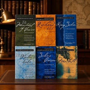 May include: Six Folger Shakespeare Library books are stacked on a table. The book titles include "The Merchant of Venice," "Richard III," "King John," "The Winter's Tale," "Julius Caesar," and "Macbeth." The books have different colored covers.