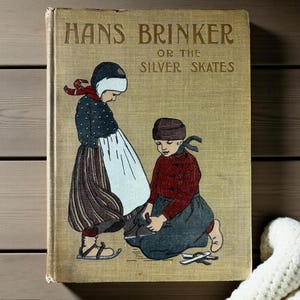 May include: Vintage book cover titled "Hans Brinker or the Silver Skates." The cover features an illustration of two children in traditional clothing. The book has a tan background with gold lettering and illustrations.