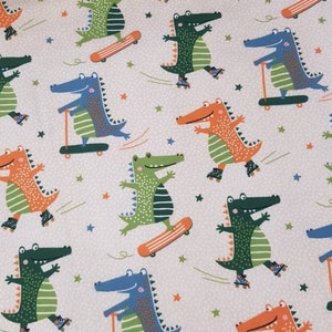 Könnte beinhalten: Stoff mit einem sich wiederholenden Muster von Cartoon-Alligatoren in verschiedenen Farben, darunter Grün, Orange und Blau. Die Alligatoren sind beim Skateboarden, Rollschuhlaufen und Rollerfahren dargestellt. Der Hintergrund ist hellgrau mit kleinen weißen Punkten und Sternen.