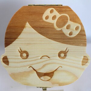 Puede incluir: Caja de madera para el hada de los dientes con un rostro de ni&ntilde;a tallado y un lazo en la cabeza. La caja es de color marr&oacute;n claro con veta de madera natural.