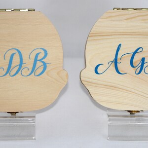 Puede incluir: Dos cajas de madera con tapas con bisagras y soportes de acr&iacute;lico transparente. Las cajas est&aacute;n decoradas con letras cursivas azules. La caja de la izquierda dice "EDB" y la caja de la derecha dice "AyB".