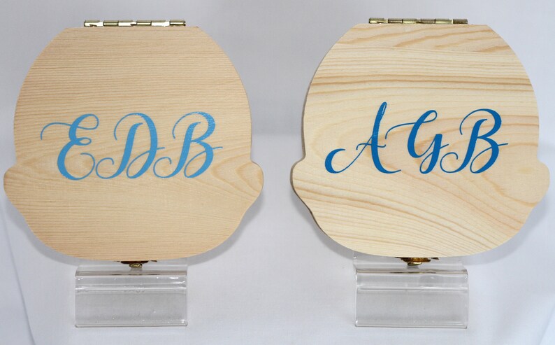 Puede incluir: Dos cajas de madera con tapas con bisagras y soportes de acr&iacute;lico transparente. Las cajas est&aacute;n decoradas con letras cursivas azules. La caja de la izquierda dice "EDB" y la caja de la derecha dice "AyB".