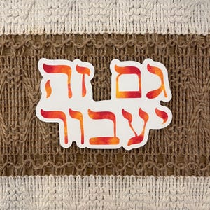 May include: A white sticker with Hebrew text in red and orange gradient colors. The sticker is placed on a textured brown and beige background. The Hebrew text is in a stylized font.