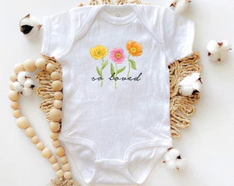 May include: White baby onesie with a graphic of three flowers in yellow, pink, and orange with green stems and leaves. The text "so loved" is printed below the flowers.