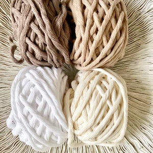 K&ouml;nnte beinhalten: Vier Kn&auml;uel aus Baumwollseil in verschiedenen Braunt&ouml;nen, Wei&szlig; und Creme. Das Seil ist dick und hat eine geflochtene Textur.