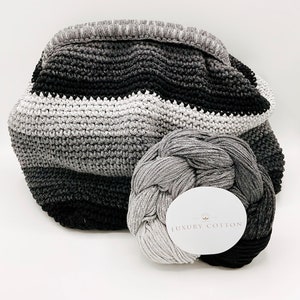 Könnte beinhalten: Eine graue und schwarze Ombre-Häkel-Tragetasche mit einer Kugel grauen Garns mit der Aufschrift "Luxury Cotton".