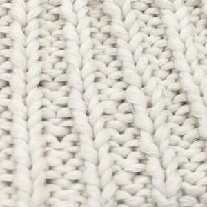 K&ouml;nnte beinhalten: Nahaufnahme eines wei&szlig;en gestrickten Stoffes mit einem strukturierten Zopfmuster.