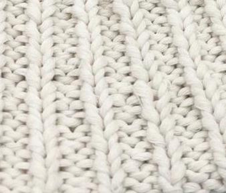 K&ouml;nnte beinhalten: Nahaufnahme eines wei&szlig;en gestrickten Stoffes mit einem strukturierten Zopfmuster.